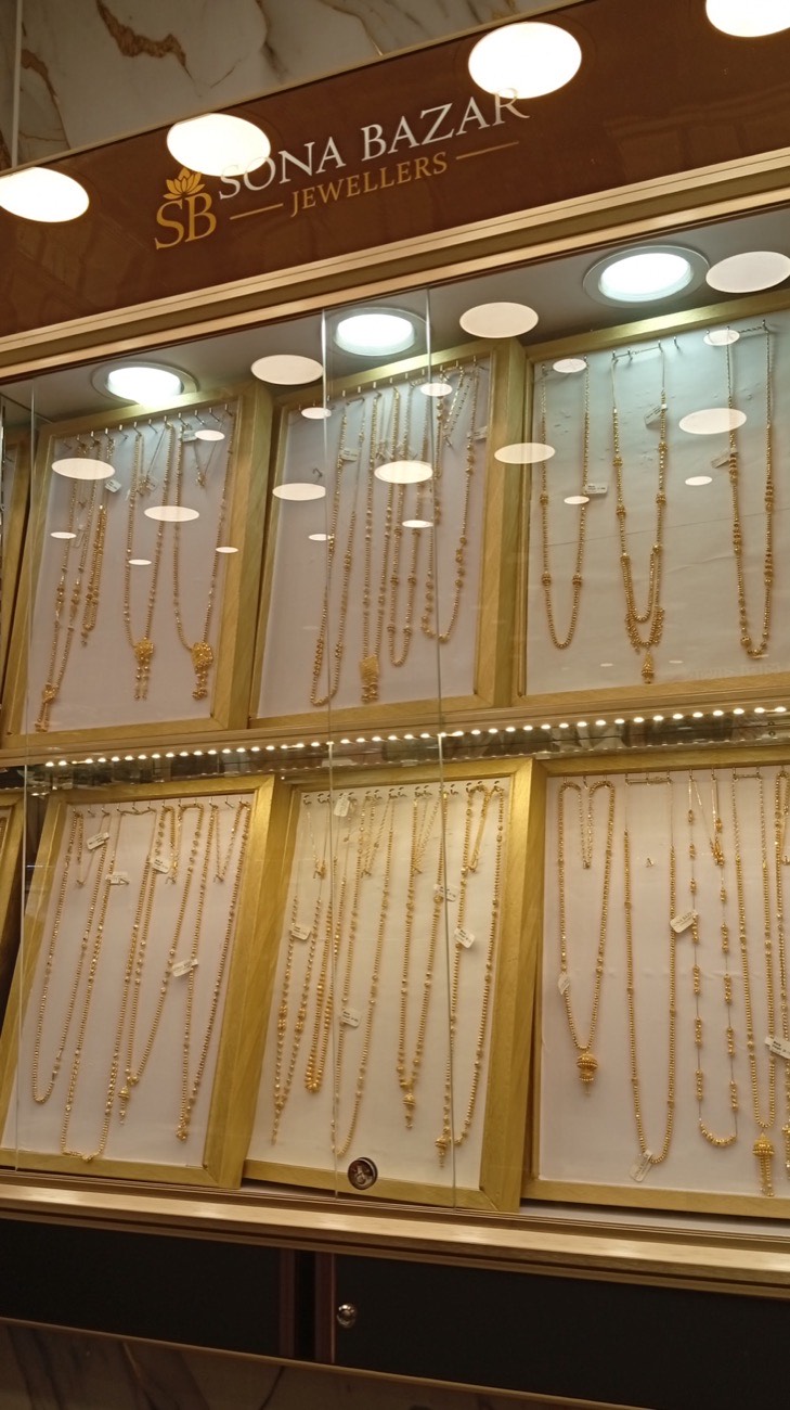 Long gold chains and haars hanging in a lit display case at Sona Bazar Jewellers
