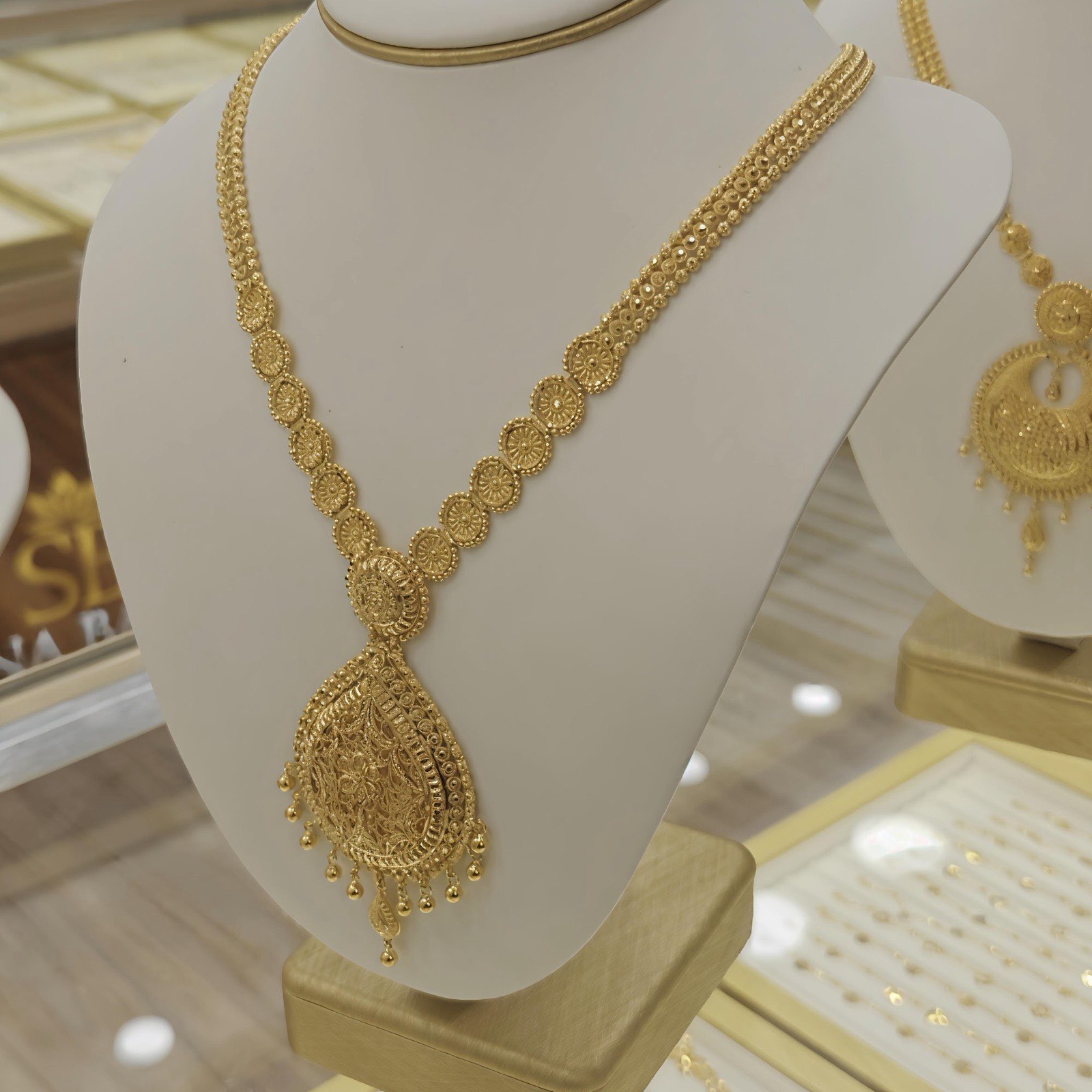 A finely worked yellow-gold necklace with a teardrop pendant and matching earrings on a display stand at Sona Bazar Jewellers, Bethnal Green